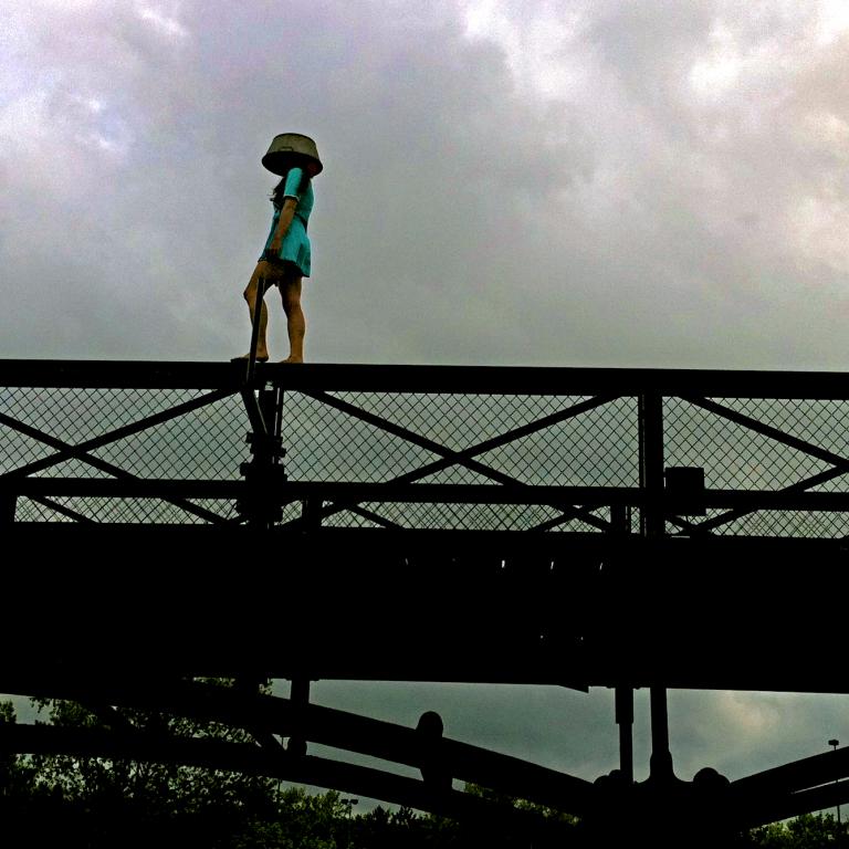 1 femme, 1 bassine sur la tête marchant sur un pont