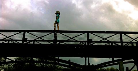 1 femme, 1 bassine sur la tête marchant sur un pont